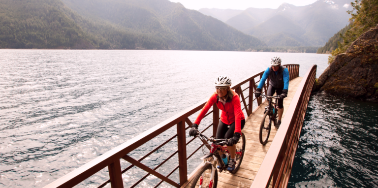 Couple biking across waterscape with moutains in the background. Symbolizing the adventurous work of journeying together in a relationship.