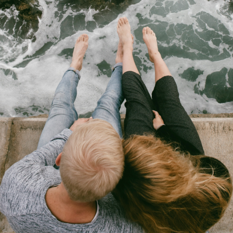 Barefoot older couple sitting together on a bridge together overlooking water below