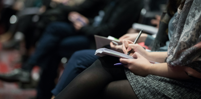 Closeup of woman taking notes in a conference settnig.